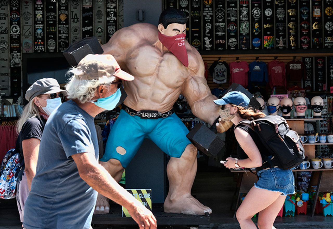 Pedestrians wearing masks walk along the strand at the Muscle beach section of Venice in Los Angeles on Friday, July 3.