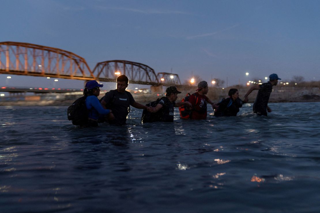Migrants link arms with each other as they wade into the Rio Grande River with intentions to cross into Eagle Pass, Texas, on February 24.
