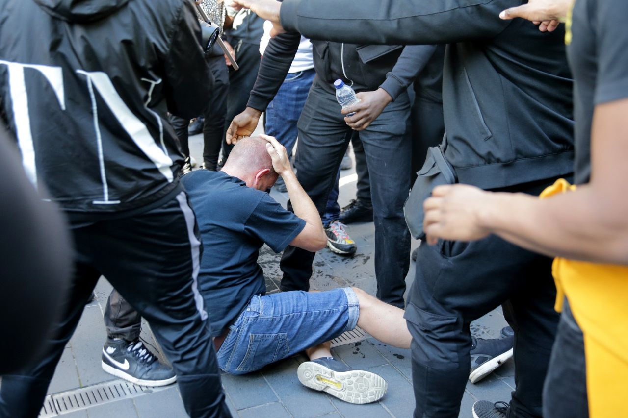 A man rubs his head as he sits on the ground after a group of men carried him away after he was allegedly attacked by some of the crowd of protesters on the Southbank near Waterloo station in London on June 13, 2020.