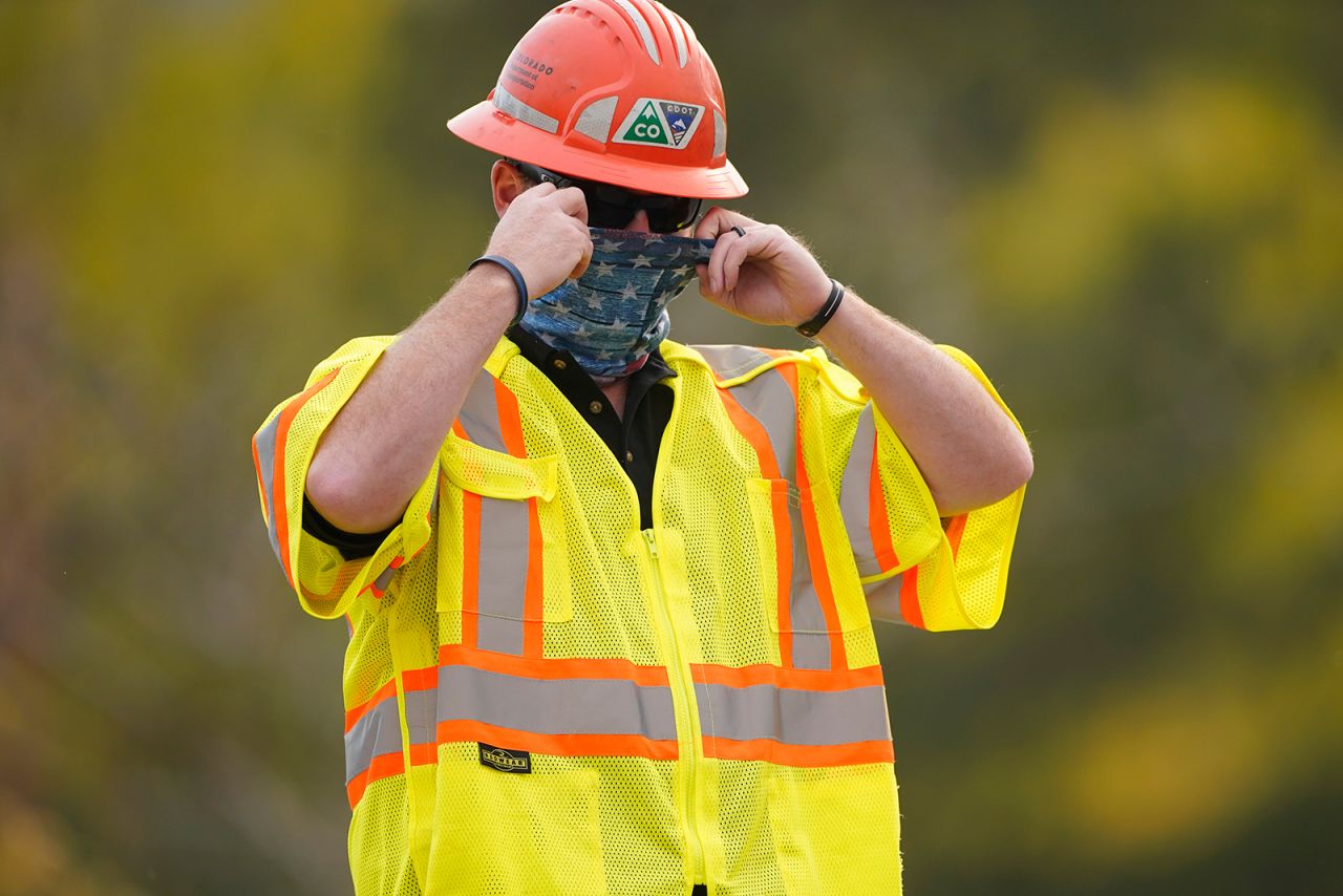 A Colorado Department of Transportation worker pulls on his face covering while staffing a roadblock into a housing area along Highway 7 as several wildfires burn in the state on October 21, in Lyons, Colorado.