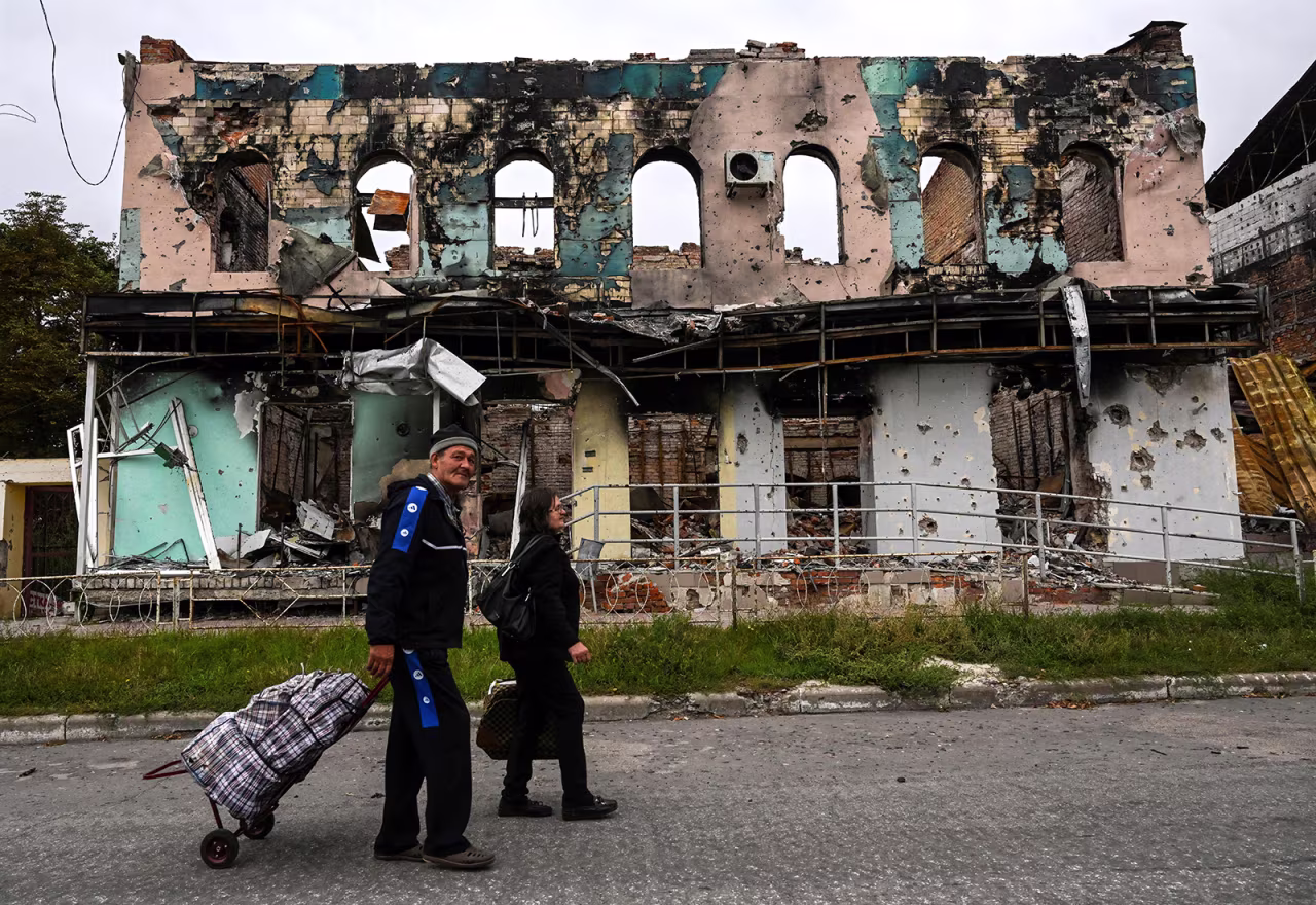 People carrying their belongings walk in front of a destroyed building in Izyum, Kharkiv Region, on September 11. 