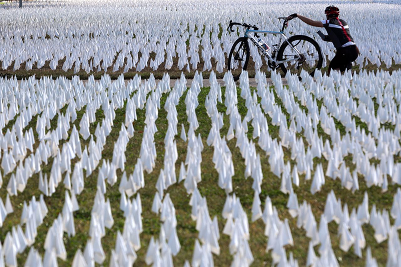 A cyclist takes pictures of the public art project “IN AMERICA How could this happen…” on the DC Armory Parade Ground October 23, 2020 in Washington, DC. The art piece, created by local artist Susanne Brennan Firstenberg, will be on display for two weeks with flags planted to represent lives that have been lost to COVID-19. 