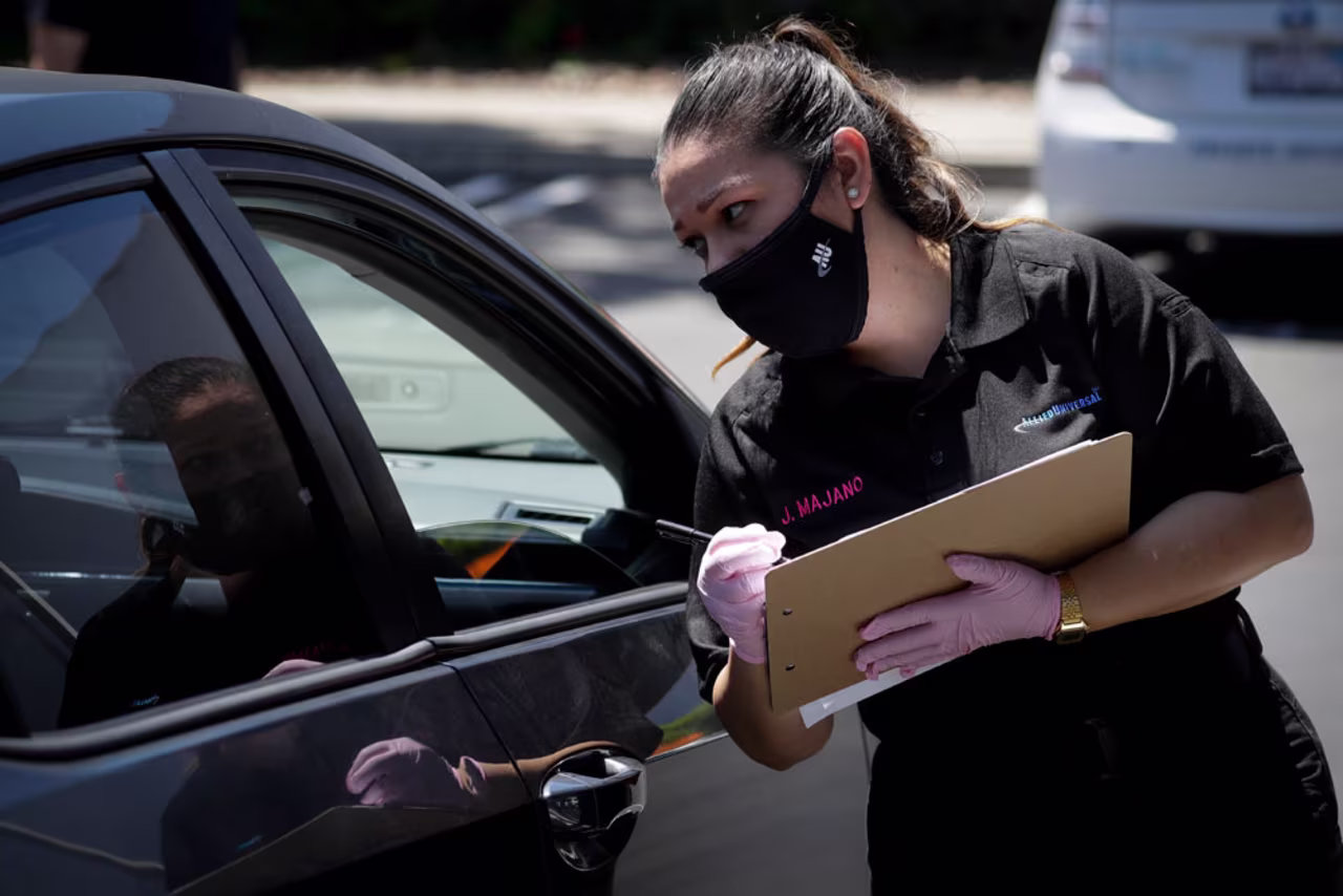 Jennifer Majano helps a job seeker fill out an application at a drive-up job fair for Allied Universal on May 6, in Gardena, California.