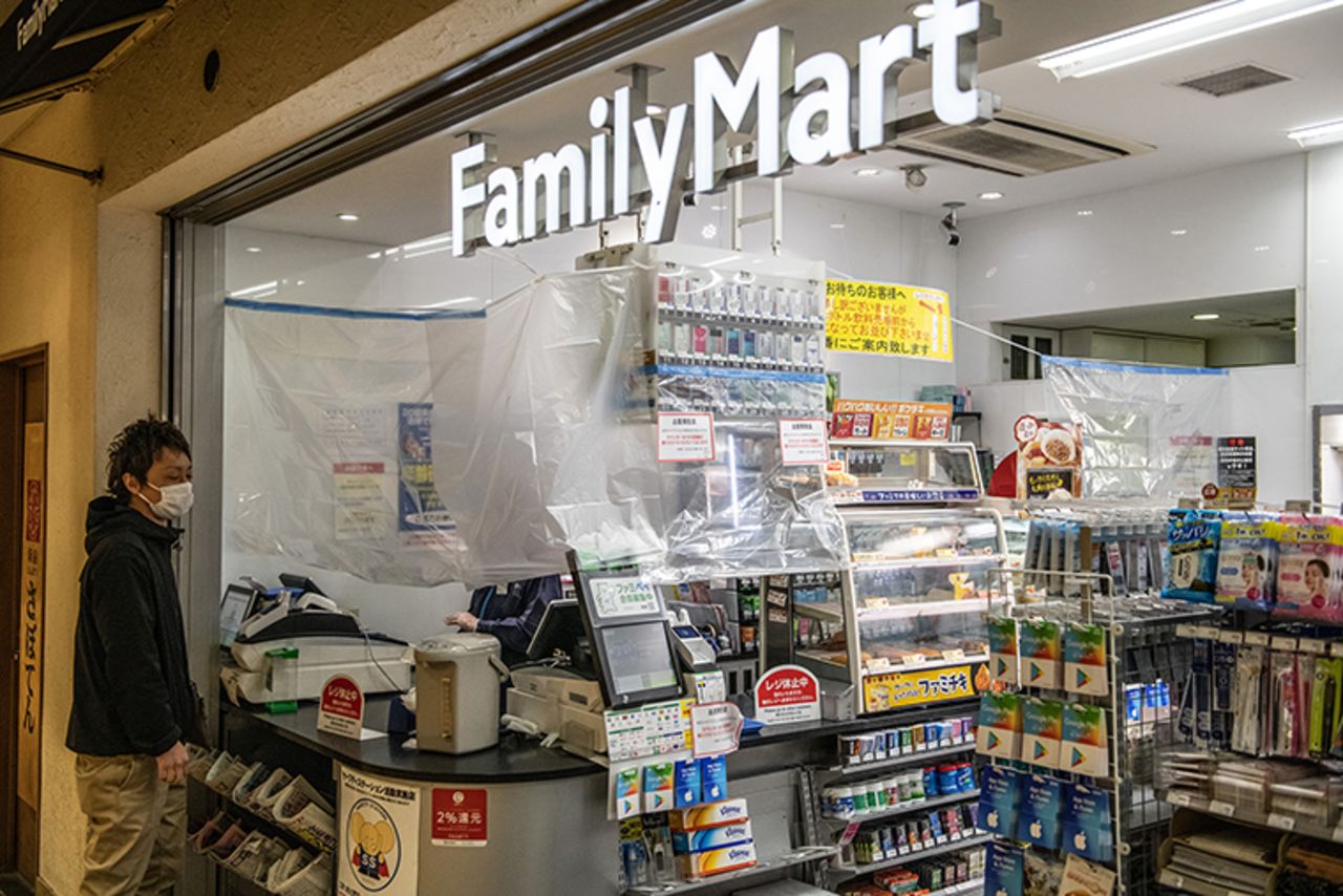 A convenience store employee serves a customer from behind plastic sheeting that has been put up to protect staff from customers who may have coronavirus, on April 14, in Tokyo.