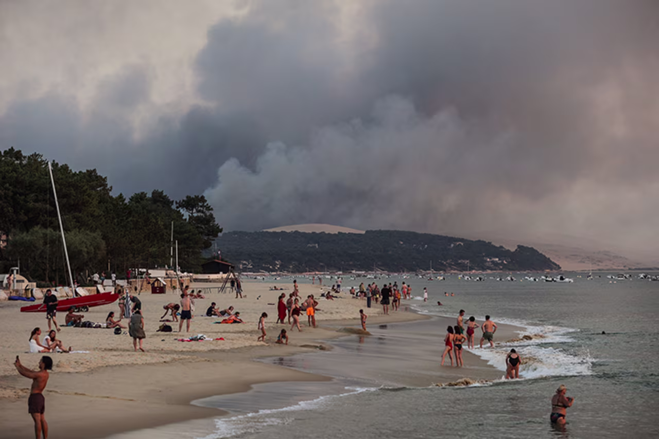 People swim on the Moulleau's beach in Arcachon, France, on Monday, July 18,  on the Moulleau's beach as the smoke rising from the forest fire in La Teste-de-Buch.