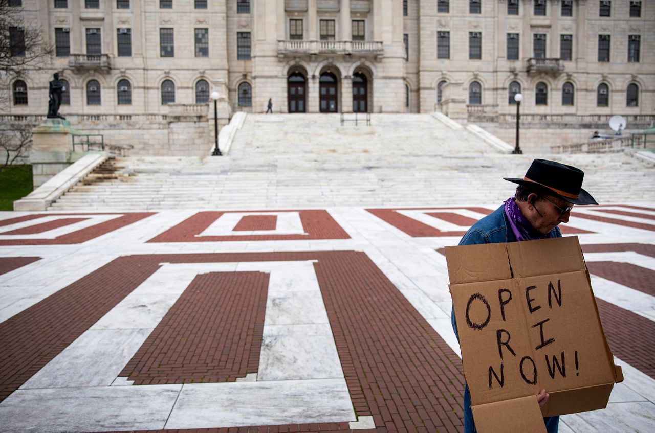 James Dunn stands outside the Statehouse with a handmade sign in favor of reopening the state economy as Rhode Island Gov. Gina Raimondo delivers her daily briefing inside, on Friday, May 1, in Providence.