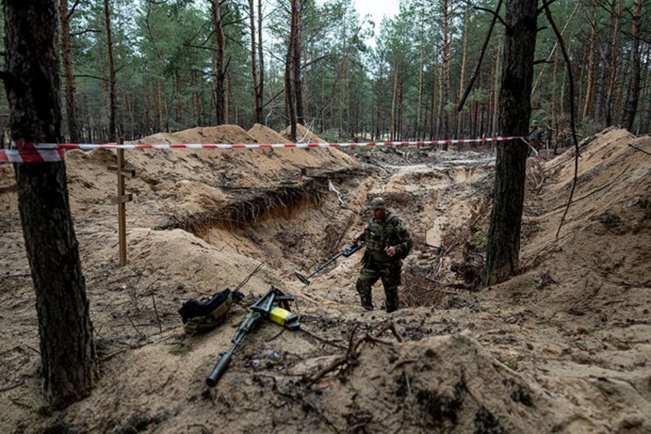 A Ukrainian serviceman uses a metal detector to inspect a mass grave in the recently retaken area of Izium, Ukraine,on Thursday, September 15.