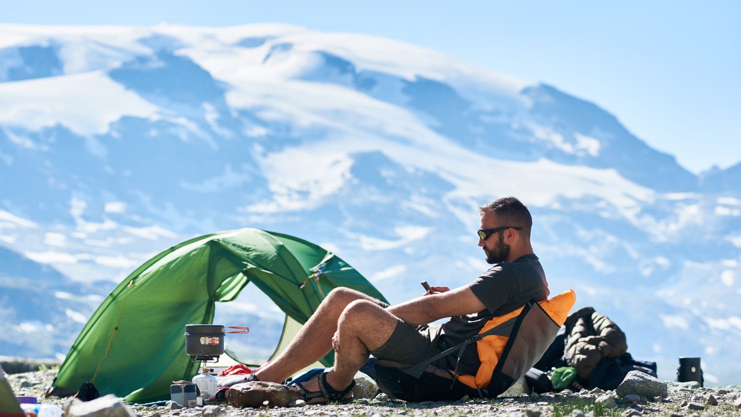 backpacker sitting next to tent with snow-capped mountains in the background