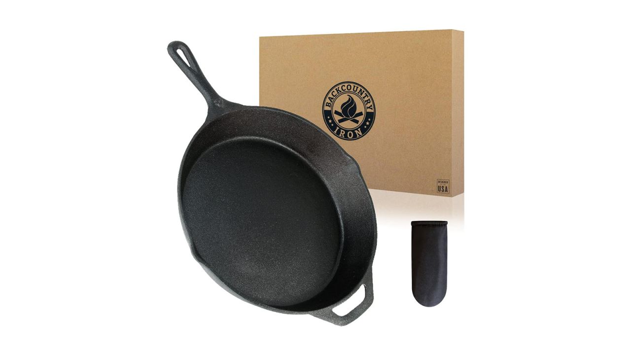 Cast iron skilled tilted in front of box and handle cover, all against white background.