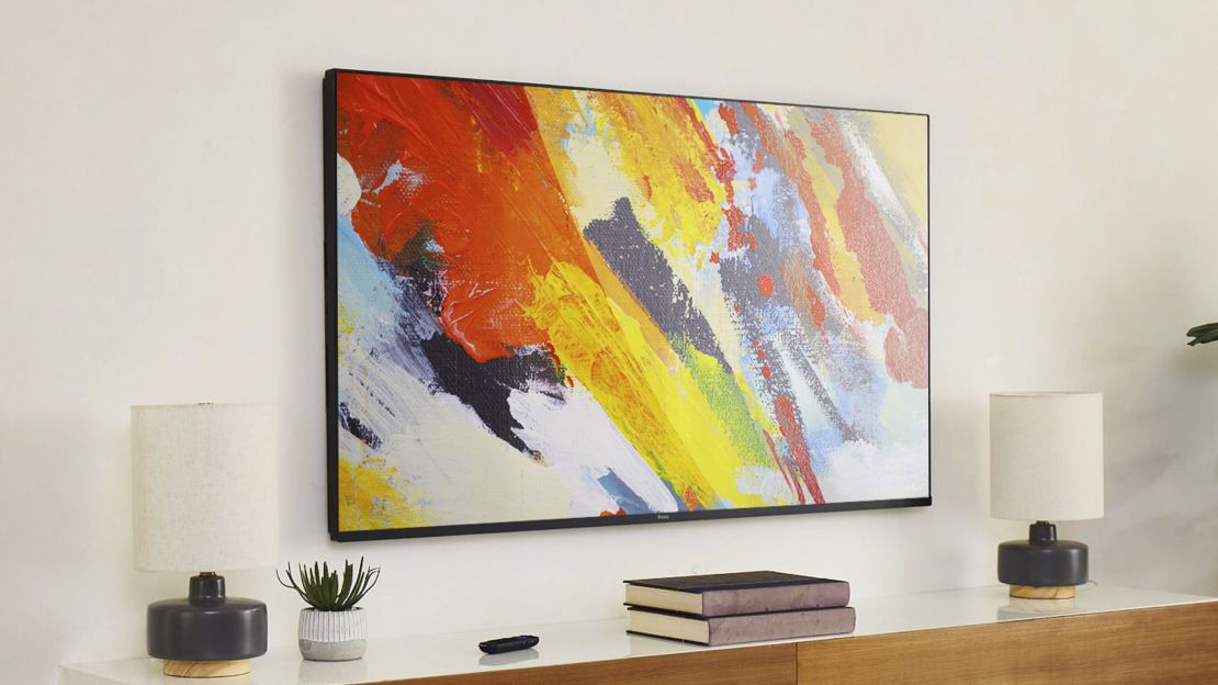 A Roku Pro Series TV showing a work of art with many streaks of paint, mounted to a wall near books and lamps.