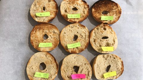 9 bagels from our toaster testing, laid out in a square pattern and labeled with the name of their respective toaster, representing the range of doneness each toaster achieved on a median setting.