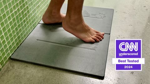 Feet stepping on stone bath mat placed at the base of a bathtub.