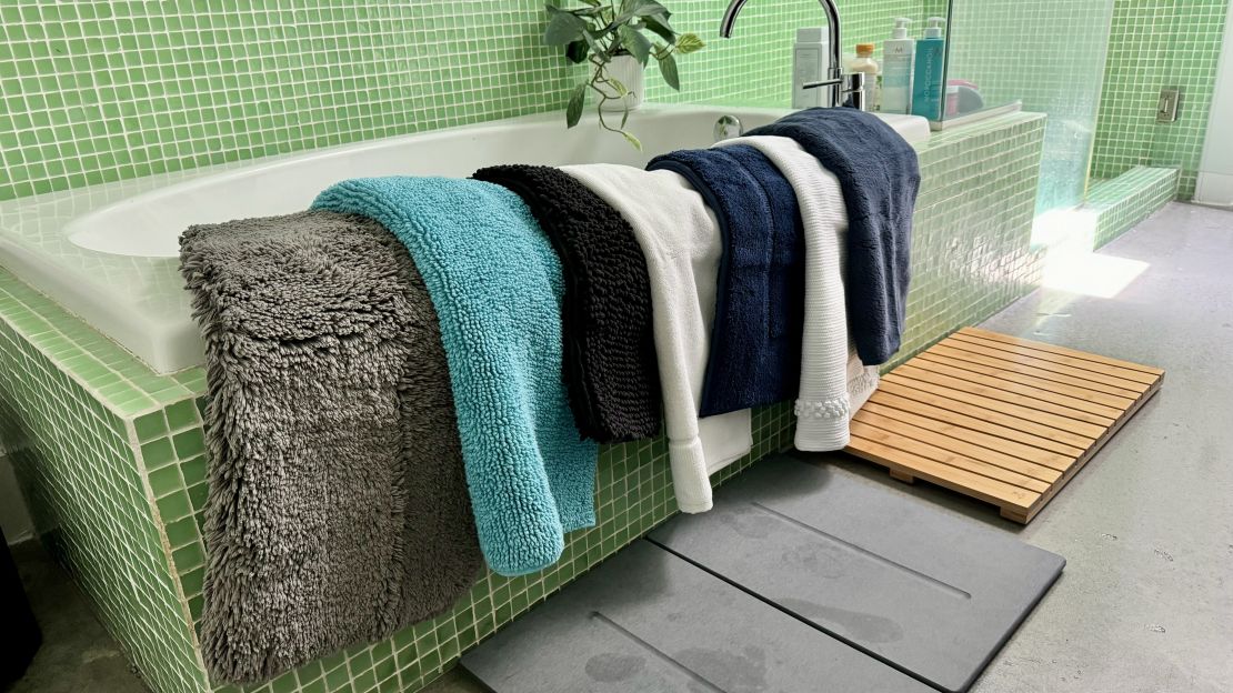 Nine bath rugs placed on and around green bathtub. 