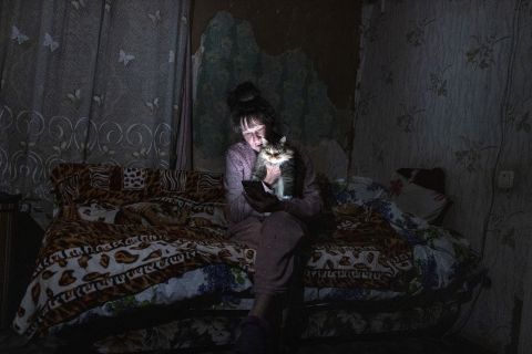 Tetyana Safonova, 61, sits with her cat Asya as she looks at her mobile phone during a power outage on October 20, 2022 in Borodyanka, Ukraine.