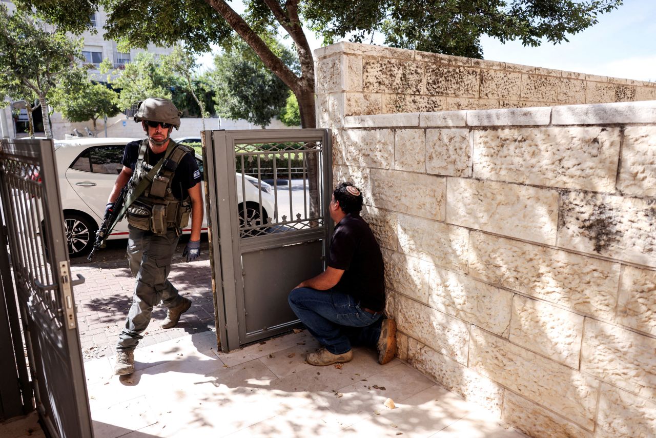 A man takes shelter by a wall as a siren sounds and rockets are launched from the Gaza Strip, in Mevaseret Zion, Israel, on October 7, 2023. 