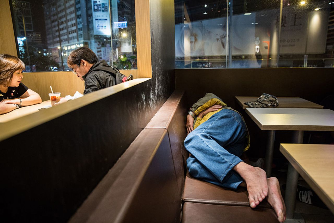 A couple sit for a meal as a man sleeps on a bench at a McDonalds outlet in the Kowloon district of Hong Kong on April 8, 2016.