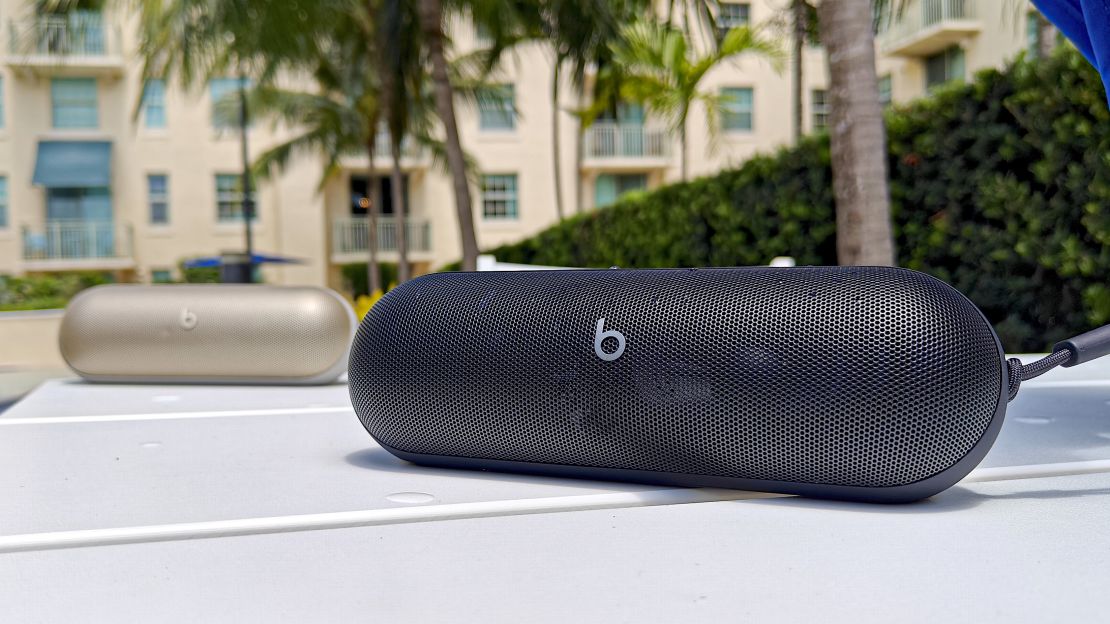 Two Beats Pill speakers on a white table with palm trees in the background.