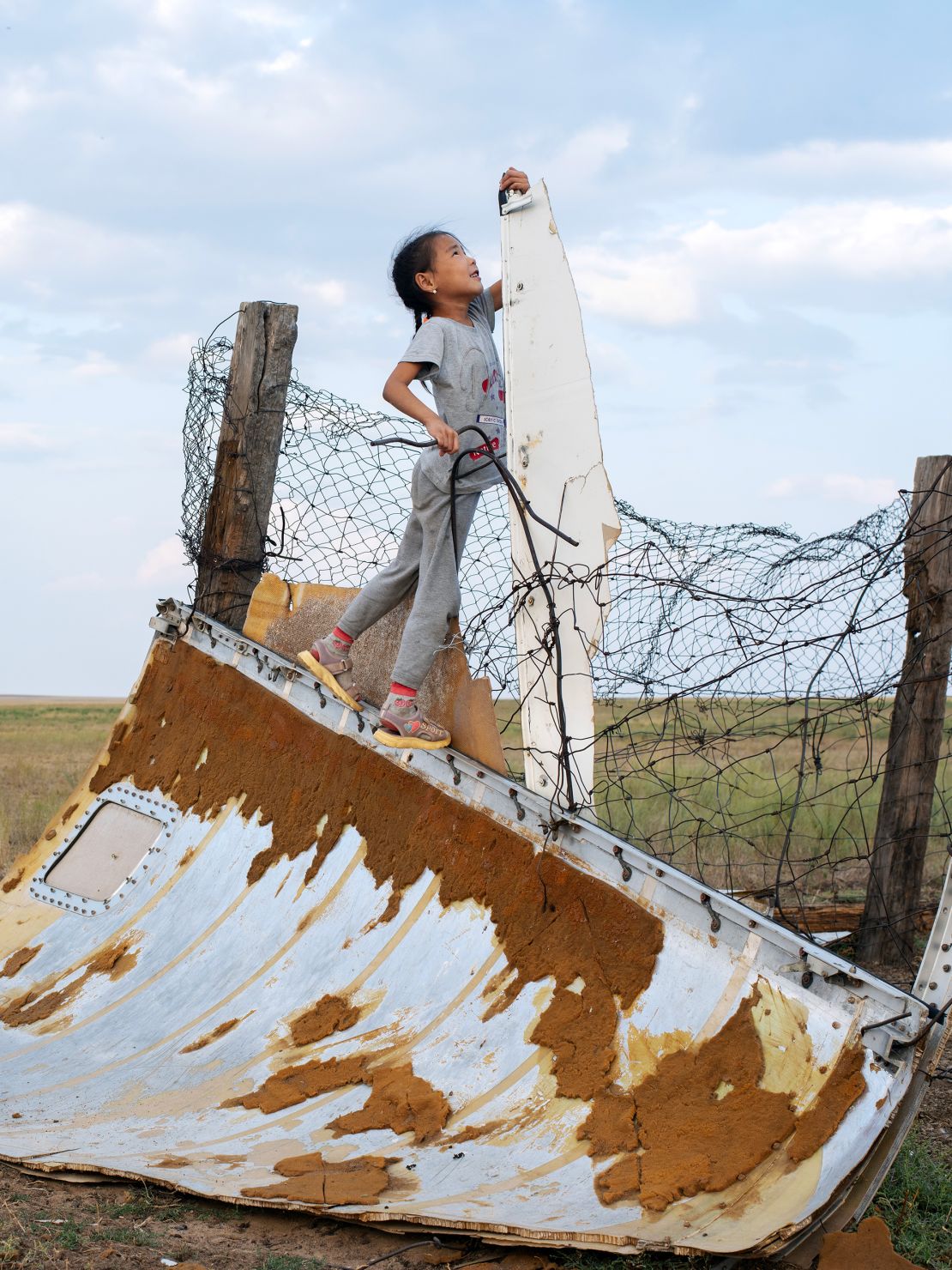 A girl plays on spacecraft debris on the grasslands.