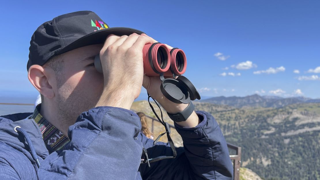 A person looking through binoculars with a mountainous view in the background. 