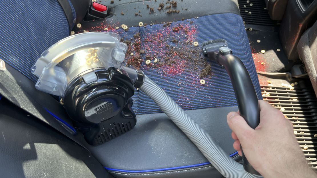 Hand holding the Black+Decker Max Flex Handheld Vacuum cleaning food from car seat.