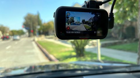 A view through a car windshield on a sunny day, with a dash cam visible upper right; the cam screen is enabled, also showing the same scene.