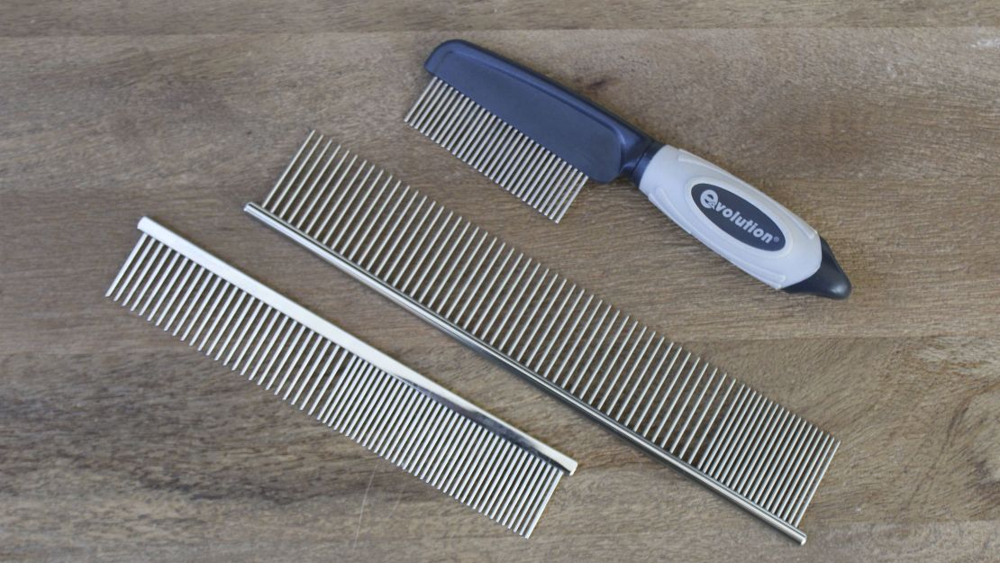 Three metal dog combs on a wooden surface.