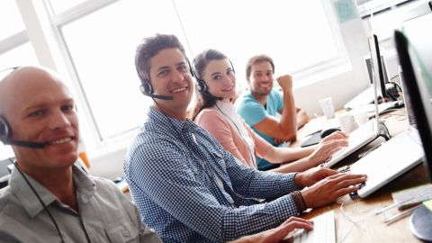 Customer service representatives smile at their desks.