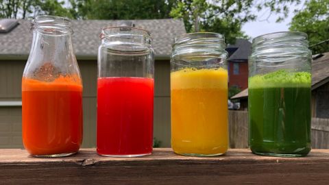Jars of freshly squeezed juice orange watermelon carrot and green juices sitting outdoors on a countertop on a sunny day