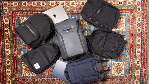 Six laptop backpacks and a MacBook on an intricate rug.
