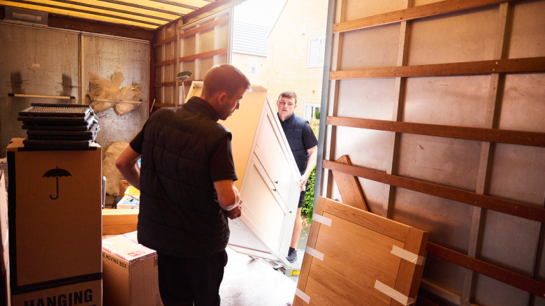 A pair of professional movers carry furniture onto a truck.