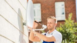 Man installs dish for satellite internet on the side of the home