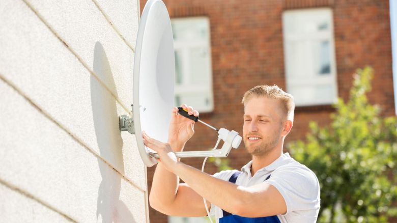 Man installs dish for satellite internet on the side of the home