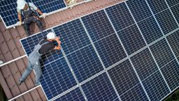 Two men install solar panels on a roof