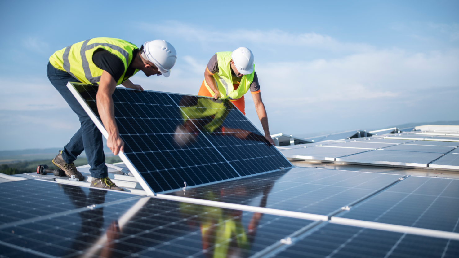 Two engineers install solar panels on a roof