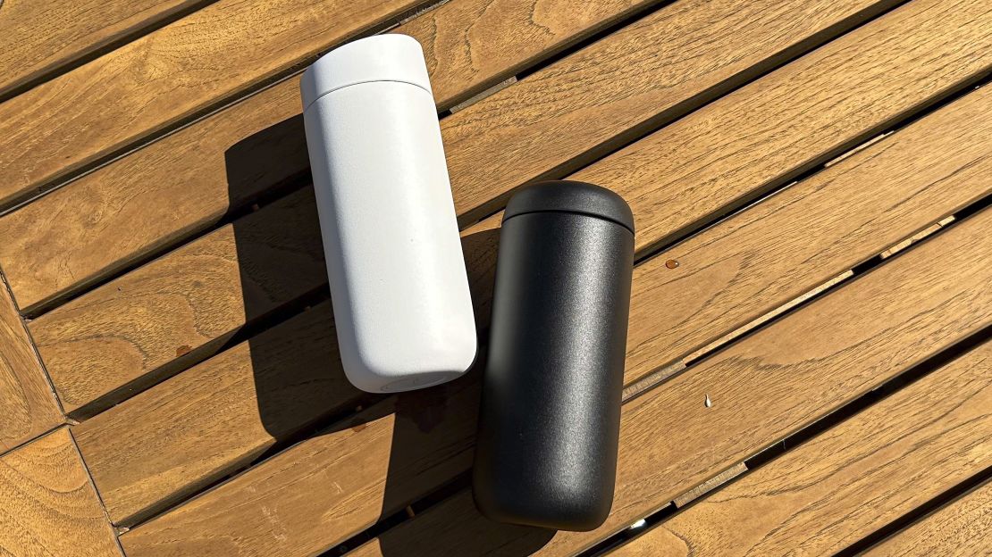 Two travel mugs placed laying next to each other on a wooden table.