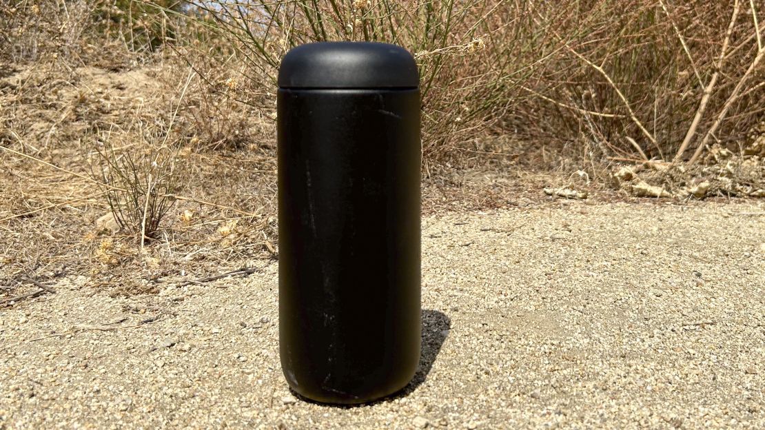 Small travel mug placed on dirt trail in front of dried brush.