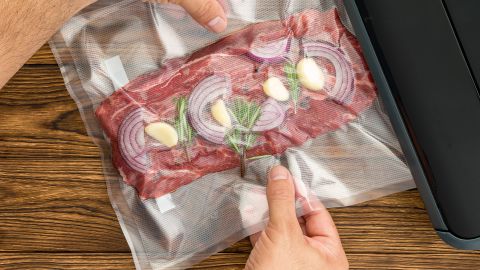 Vacuum sealing a bag containing beef topped with red onions, garlic and rosemary.