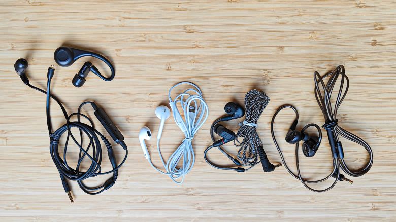 Four pairs of wired earbuds on a wooden surface.