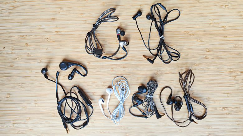 Seven pairs of wired earbuds on a wooden surface.