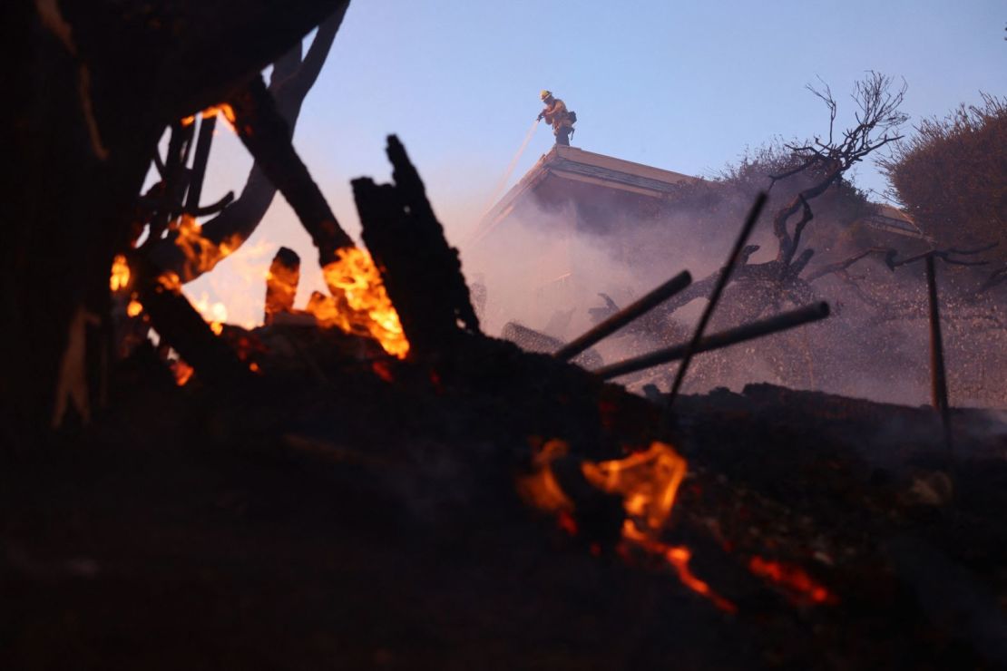 Un bombero rocía un punto caliente mientras el fuego arde en Pacific Palisades.