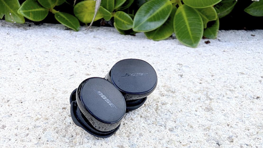 Bose QuietComfort Earbuds on the ground next to greenery.