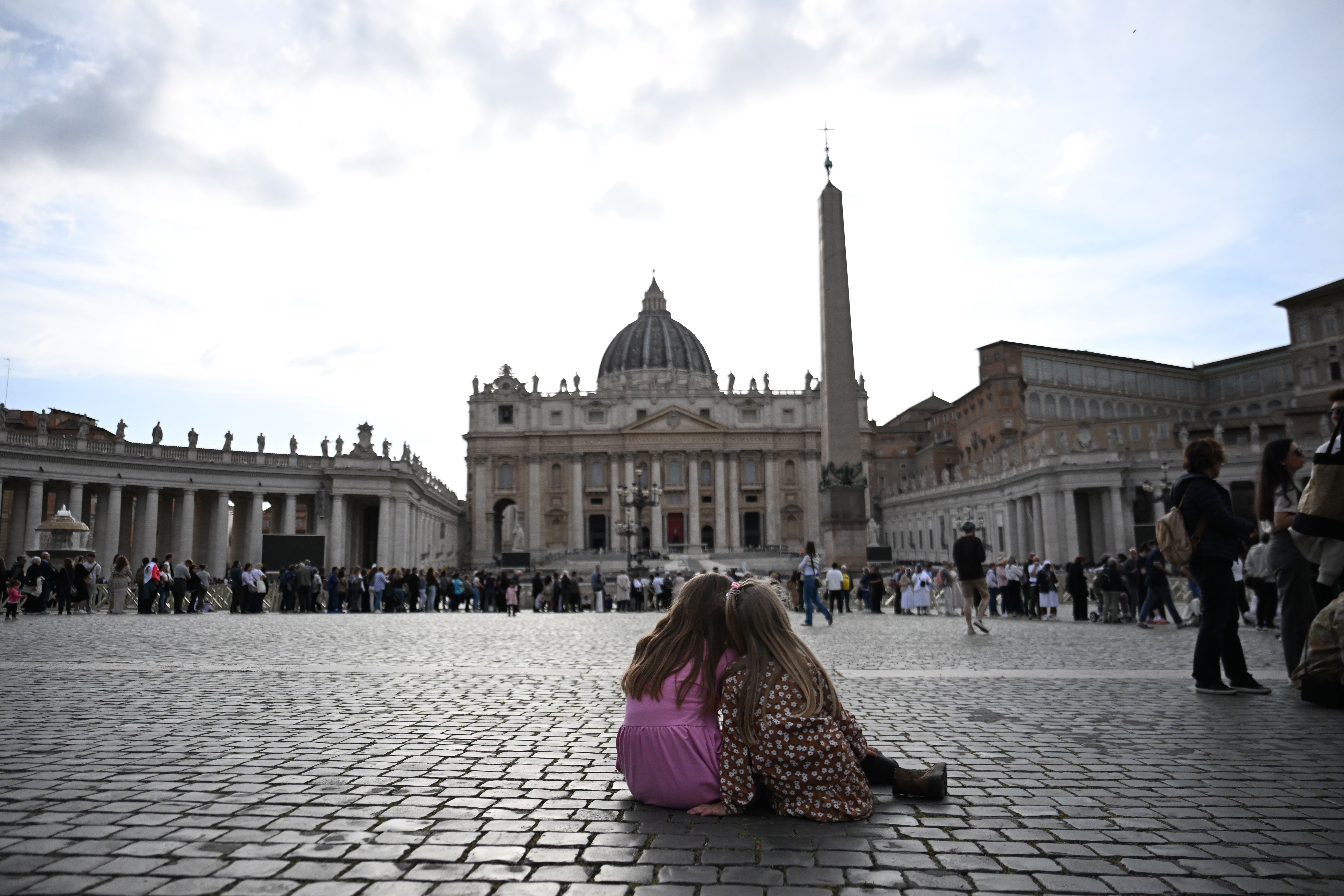 Two girls rest in St. Peter's Square as their family waits in line to view the pope's body.