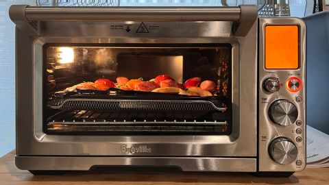The Breville Joule Smart Oven, cooking a meal of potato, onion, and sausage, on a wooden kitchen island.