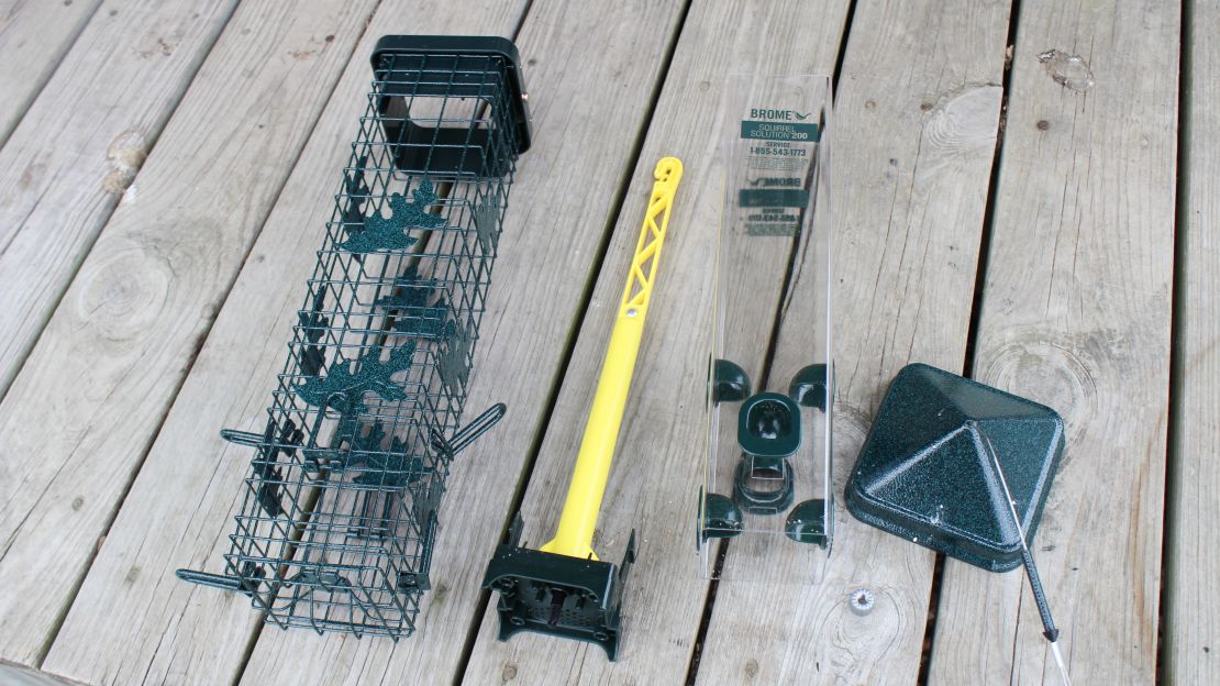 The pieces of the Brome Squirrel Solution 200 bird feeder are disassembled and laid out on a wooden deck.