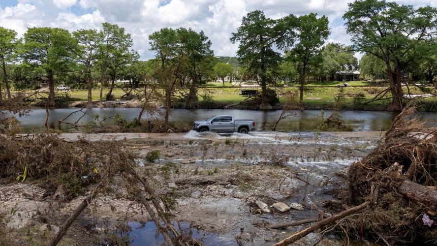 A vehicle drives through a road flooded by the waters of the Guadalupe River in Hunt, Texas, on July 9.