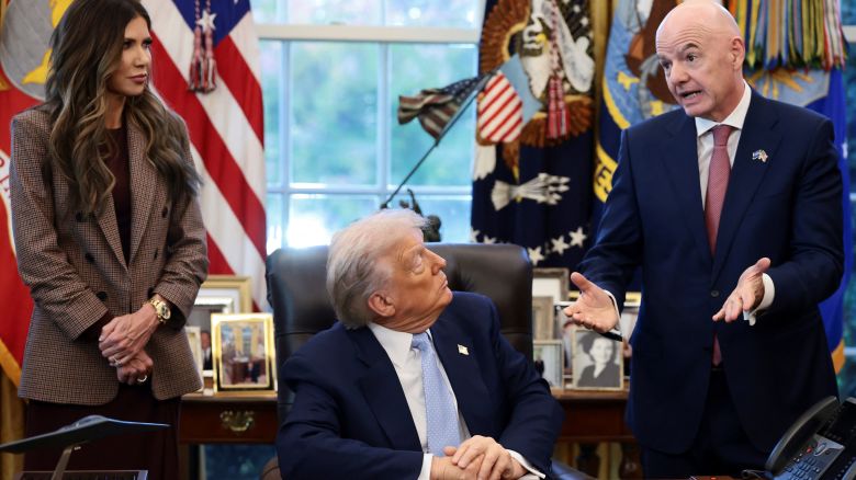 President Donald Trump sits while FIFA President Gianni Infantino and U.S. Homeland Security Secretary Kristi Noem stand by his side, as he meets with the White House Task Force on the FIFA World Cup 2026 in the Oval Office at the White House in Washington, D.C., U.S., November 17, 2025.