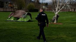 With Fruitdale Elementary School in the background, a Grants Pass police officer walks to check on a homeless person after relatives asked for a welfare check at Fruitdale Park on Saturday, March 23, 2024, in Grants Pass, Oregon.