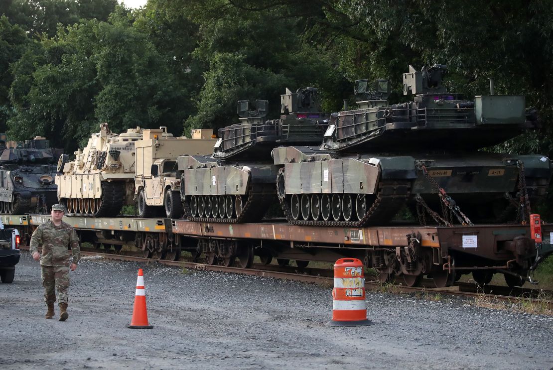 This 2019 photo shows two M1-A1 Abrams tanks and other military vehicles sit on guarded rail cars at a rail yard in Washington, DC.