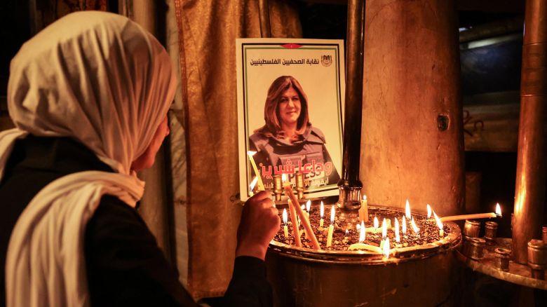 A woman lights a candle in front of a poster depicting veteran Al-Jazeera journalist Shireen Abu Akleh, who was shot dead while covering an Israeli army raid in Jenin, at the the Church of the Nativity in the West Bank biblical city of Bethlehem on May 11, 2022. 
