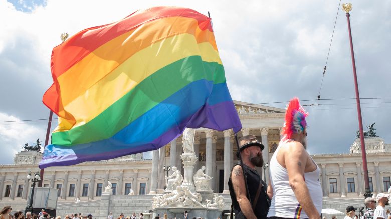 Pride parade participants  with an LGBTQIA+ flag in front of the Austrian Parliament on the Ringstrasse in Vienna on June 17, 2023.